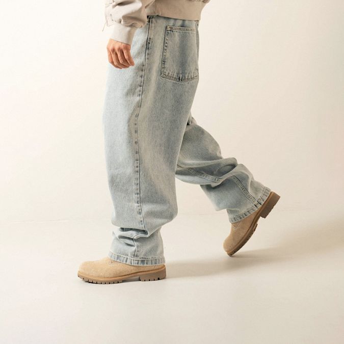 Person walking while wearing light-wash baggy jeans and beige suede work shoes, shown from the waist down.