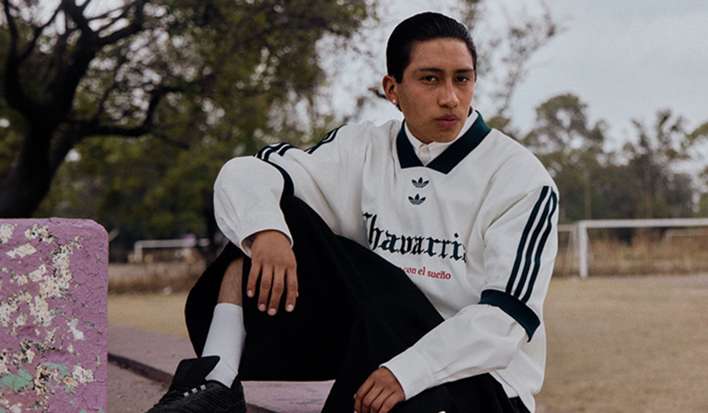 adidas Originals x Willy Chavarria outfit featuring a white long-sleeve top with black stripes and logo details, styled with black shorts and sneakers, shown in an outdoor setting.