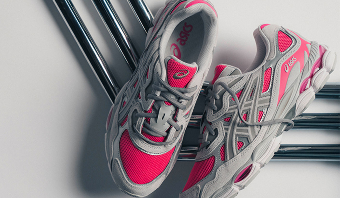 Pair of ASICS GEL-NYC sneakers in grey and pink, displayed on chrome tubes, highlighting the layered mesh upper and cushioning-focused running-inspired design.
