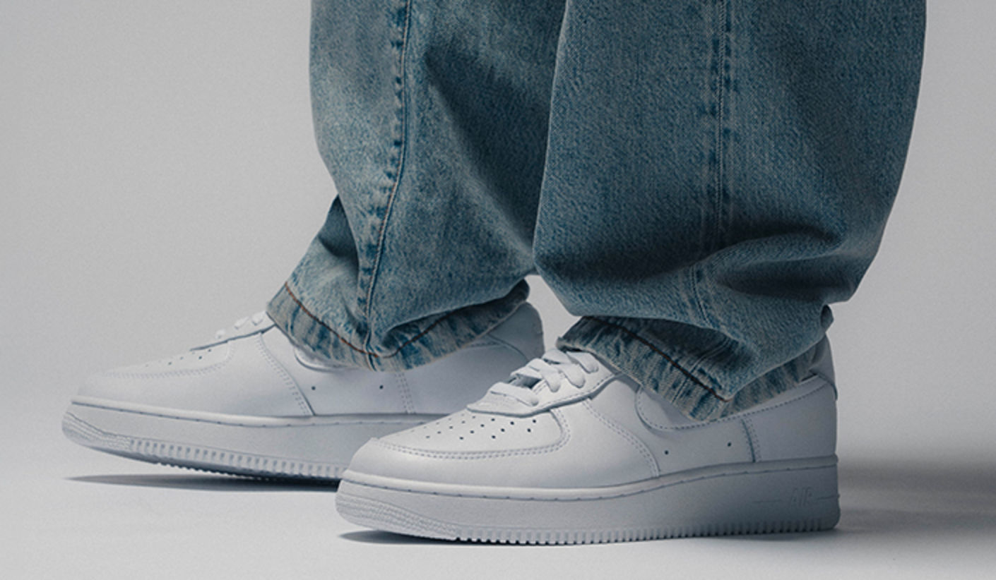 Close-up of the Nike Air Force 1 “Triple White” (2001 Shape) in all-white leather, worn with loose blue denim jeans, highlighting the classic low-top silhouette and clean minimalist design.
