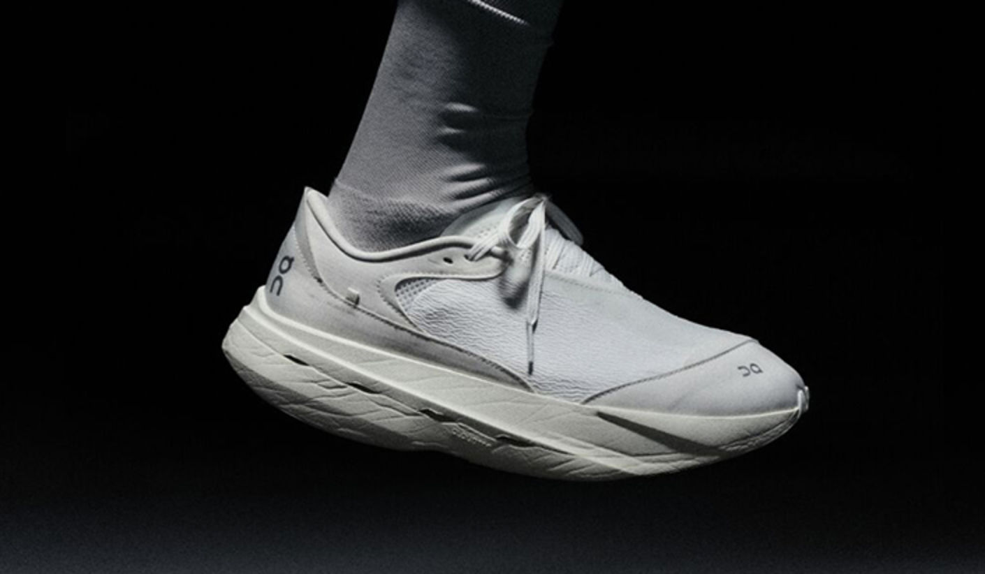 Close-up of an On x PAF running shoe in all-white, worn with white socks, shown in a floating pose against a dark background.