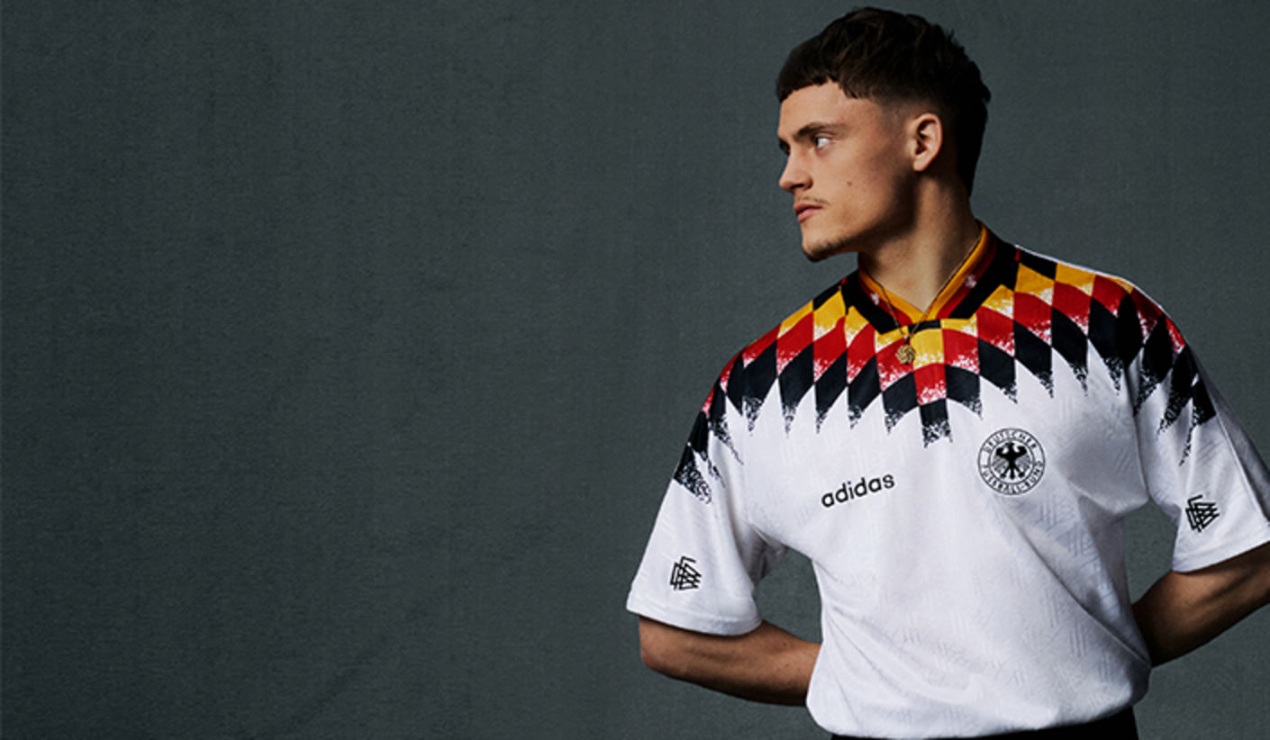 Person wearing a vintage Adidas Germany national team jersey with black, red, and gold pattern, standing against a gray background and facing sideways. Geben Sie Ihr Feedback zu BizChat ab.