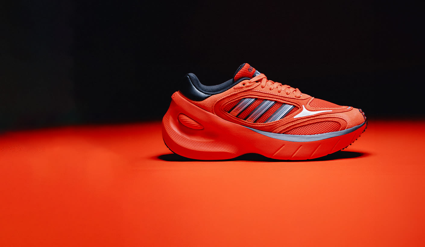 Bright red Adidas sneaker with futuristic chunky sole, metallic three stripes, and black inner lining, showcased on a red surface with a dark gradient background.