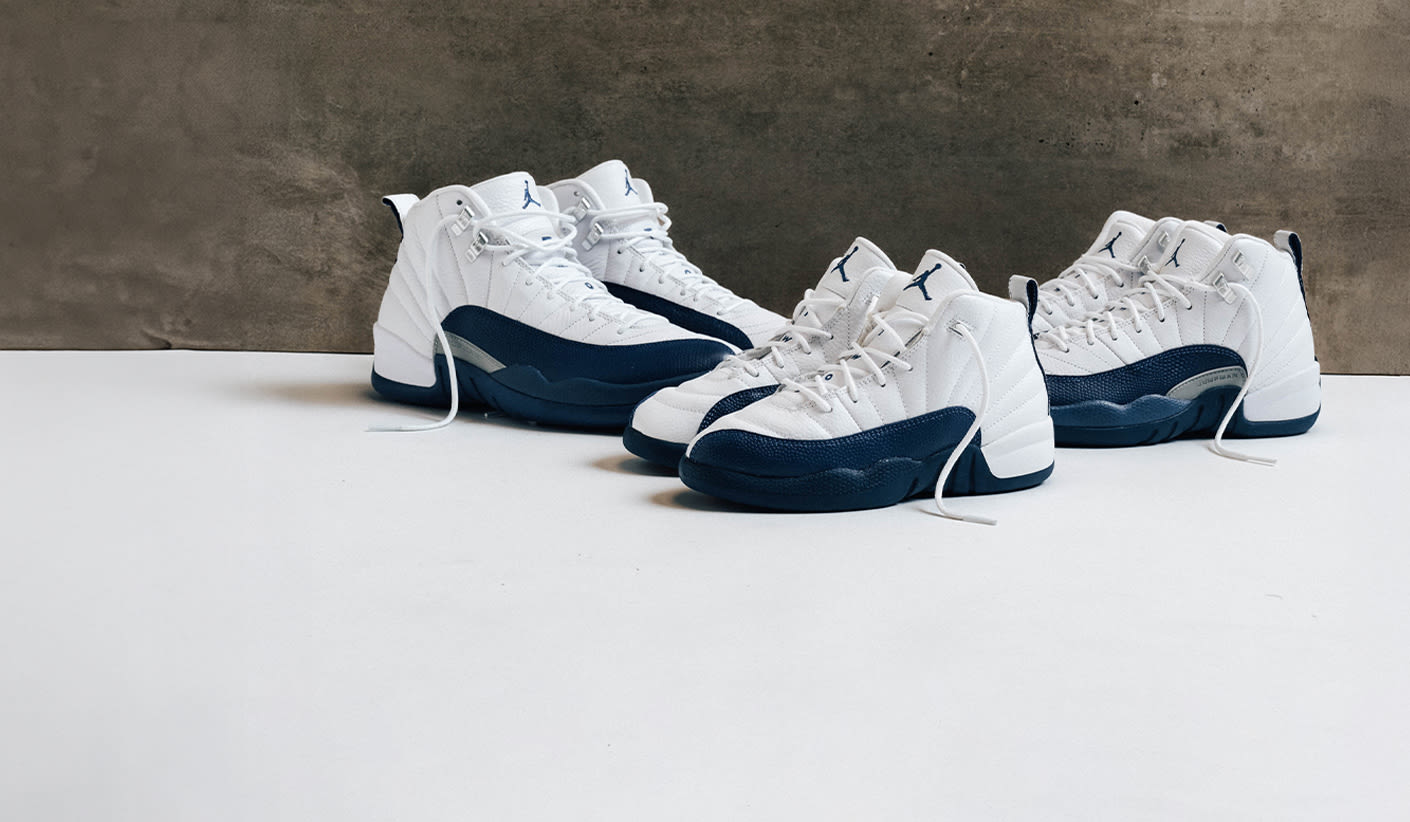 Three pairs of Air Jordan 12 sneakers in white and navy blue colorway displayed on a white surface with a concrete background.
