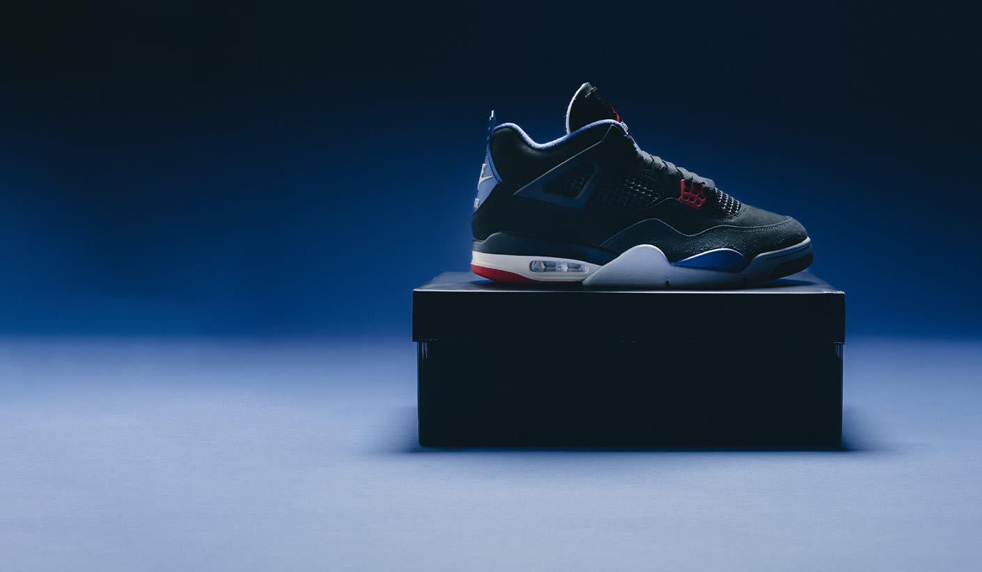 A single Air Jordan 4 sneaker in black, red, white, and blue colorway displayed on top of a closed black shoebox, set against a dark blue gradient background with dramatic lighting.