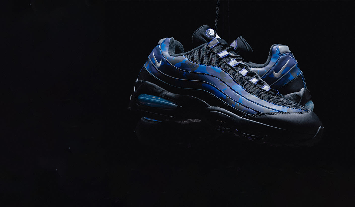 "Nike Air Max 95 sneakers in black with blue camo accents, displayed against a dark background.