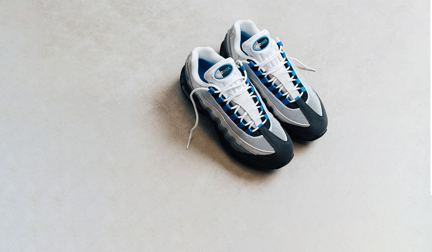 Pair of Nike Air Max 95 sneakers in white, grey, black, and blue, placed on a light-colored floor.