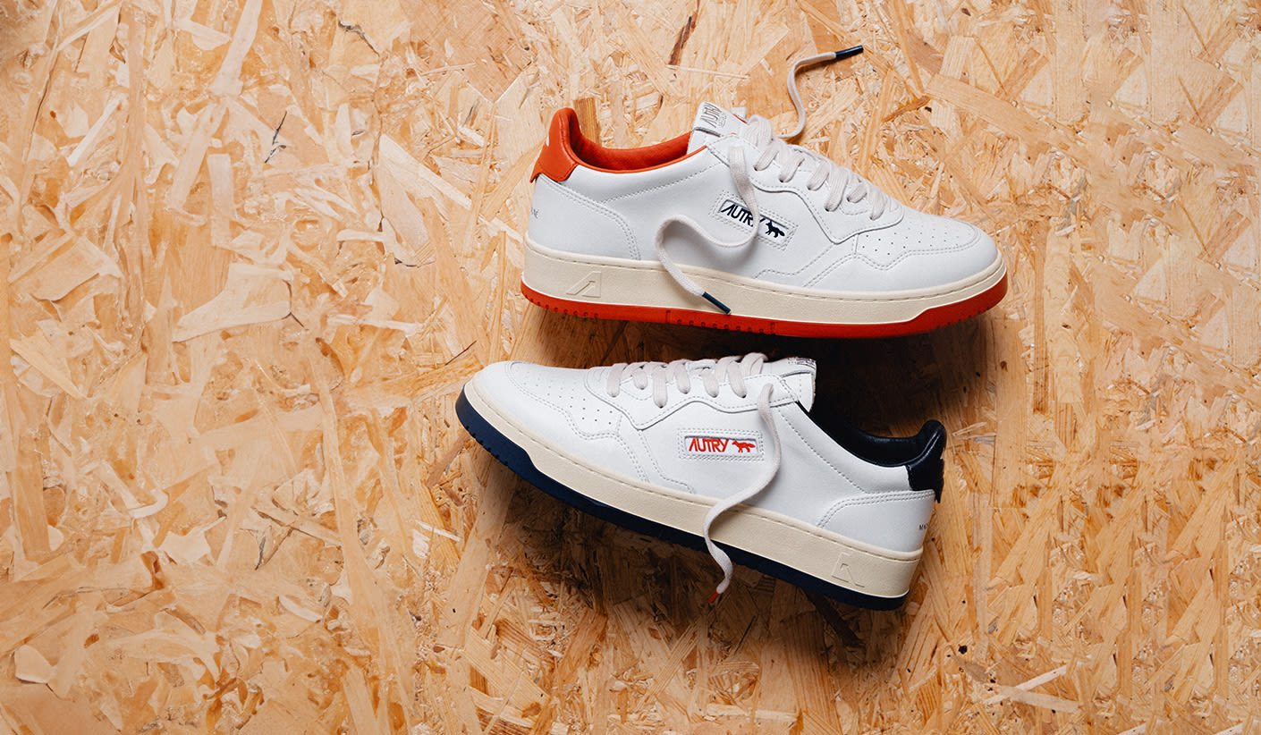 "Two pairs of white Autry sneakers with colored details – one with red accents and the other with navy – displayed on a wooden textured surface."