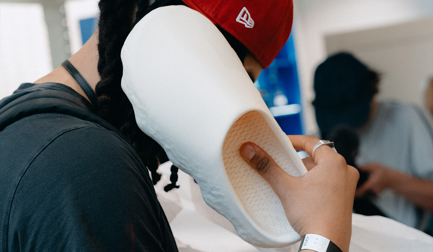 A person wearing a red cap holds a large white shoe sole against their ear as if using it like a phone.