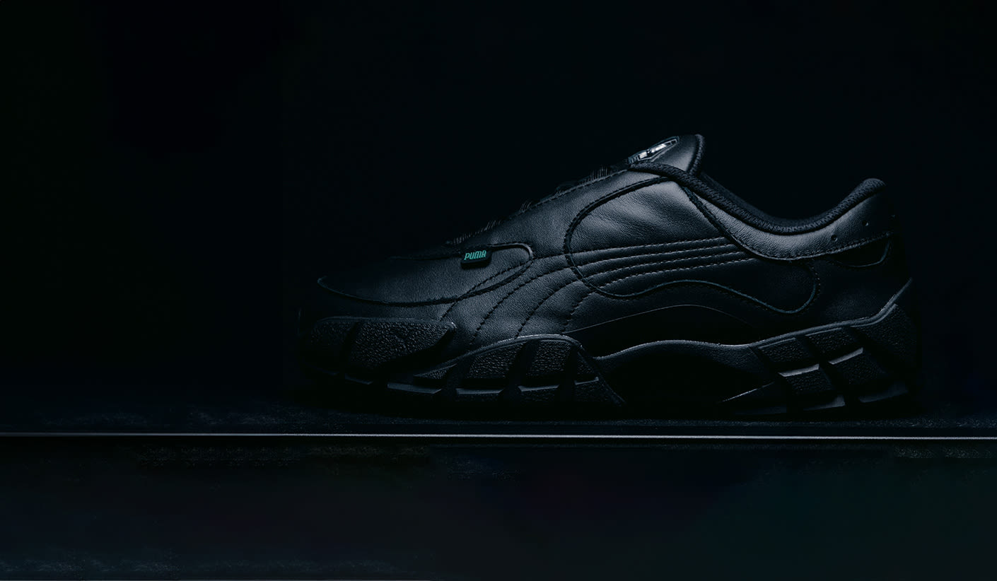 Black leather Puma sneaker in side view on a dark background, minimal lighting highlighting the shoe’s details.