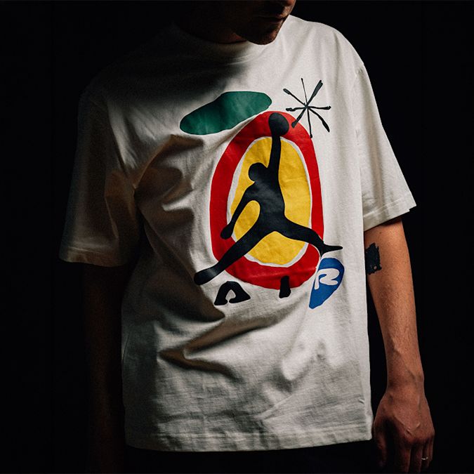 Jordan Brooklyn “Miro 85” T-shirt with colorful abstract graphic and Jumpman logo, shown in a dark, studio-lit close-up.