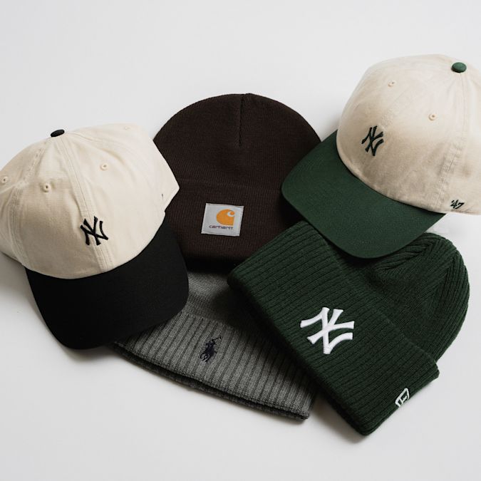 Flat lay of four jackets in different styles and colors: a black puffer jacket with Nike ACG logo, a dark green corduroy Carhartt jacket, a brown Carhartt hooded work jacket, and a black hooded jacket.