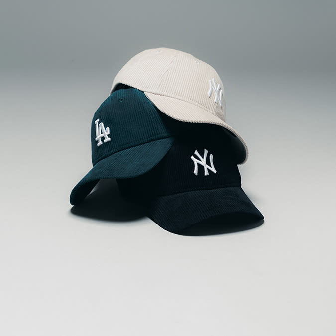 A stack of three corduroy baseball caps with embroidered logos — a beige New York Yankees cap, a dark green Los Angeles Dodgers cap, and a black New York Yankees cap.