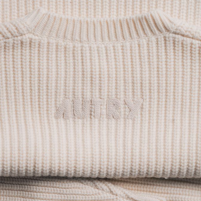 Close-up of a cream-colored ribbed knit sweater featuring an embroidered "AUTRY" logo on the chest and a ribbed crew neckline.