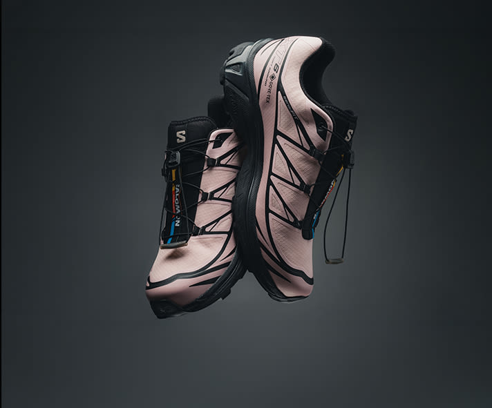 Pair of light pink Salomon XT-6 Gore-Tex trail running shoes with black detailing and Quicklace system, displayed floating against a dark gradient background.