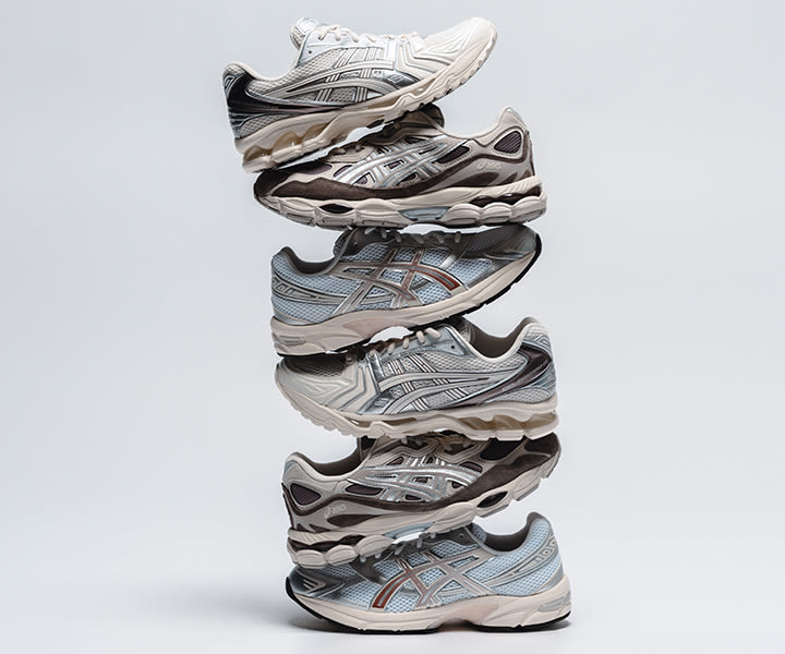 Multiple pairs of ASICS Gel-Kayano 14 sneakers arranged in a vertical lineup against a neutral background, featuring mesh and metallic overlays in white, silver, beige, and soft blue tones with layered, retro running design details. Geben Sie Ihr Feedback zu BizChat ab.