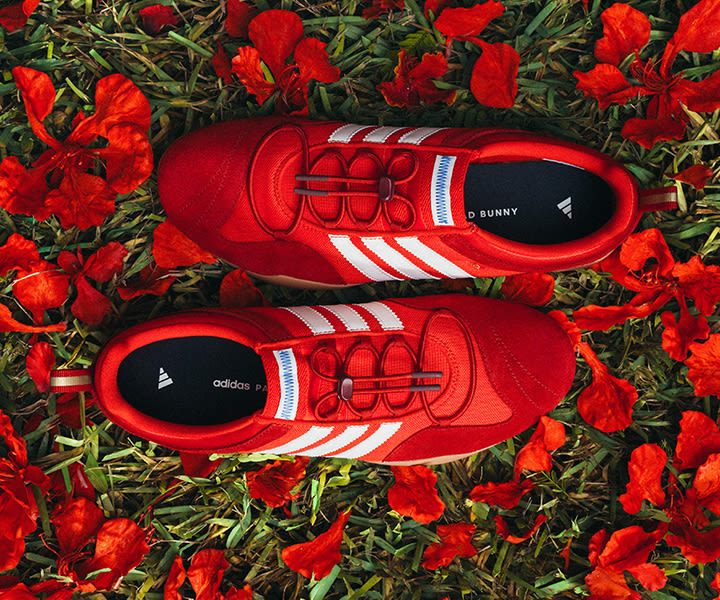 Top view of red adidas x Bad Bunny Ballerina sneakers with white three stripes, placed on grass surrounded by bright red flower petals. Geben Sie Ihr Feedback zu BizChat ab.