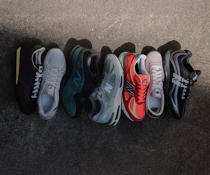 Row of New Balance sneakers in various colors and styles, including grey, green, red, pink, and black, arranged on textured ground under natural light, showcasing new arrivals.
