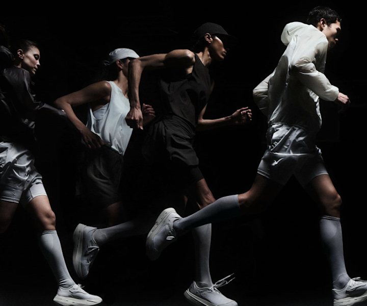 Group of runners wearing the On x POST ARCHIVE FACTION collection, moving through a dark studio setting. Technical silhouettes, monochrome tones, and performance footwear create a futuristic running aesthetic.