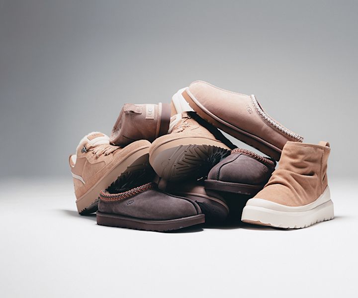 "A pile of various UGG shoes in soft neutral tones including beige, tan, and brown, arranged on a white surface with a gray gradient background. The styles include slippers, sneakers, and ankle boots, made of suede and featuring plush or rugged soles."