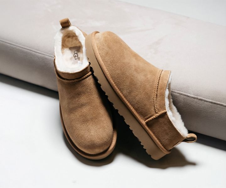 Pair of tan UGG Classic Ultra Mini boots with a suede exterior and white fleece lining, placed on a light-colored surface.