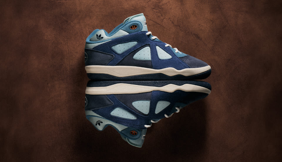 adidas x Bad Bunny Badbo 1.0 "Night Navy" sneaker in dark navy and light blue suede and leather, shown in side profile against a textured brown background.
