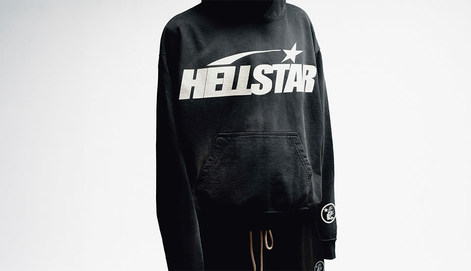 Person wearing a black Hellstar hoodie with an oversized white Hellstar logo across the chest, styled with black pants against a white background.