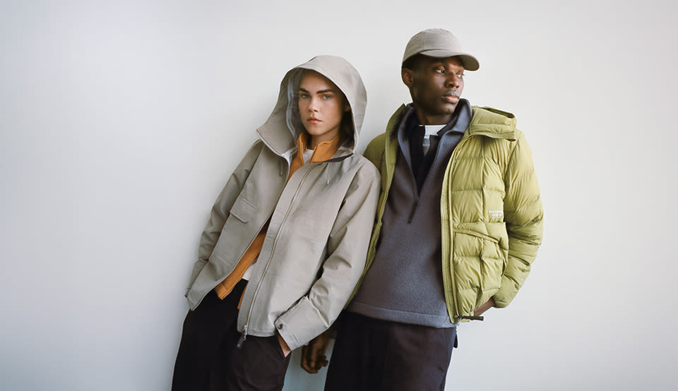 Two models wearing layered Pas Normal Studios outerwear, including a light shell jacket and an insulated puffer jacket, styled for cool-weather cycling and urban exploration.