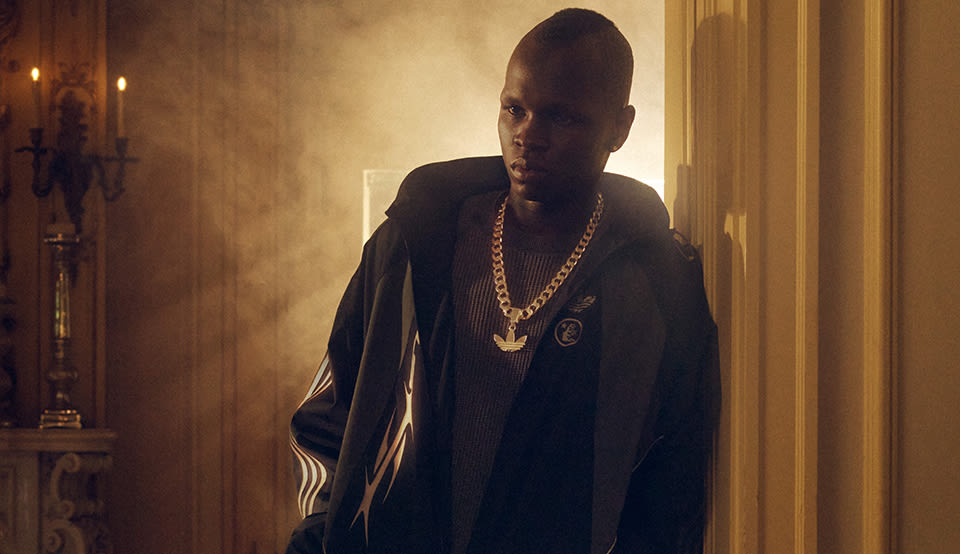 Person wearing apparel from the adidas x Hellstar collaboration in a dimly lit interior with warm lighting and atmospheric smoke.