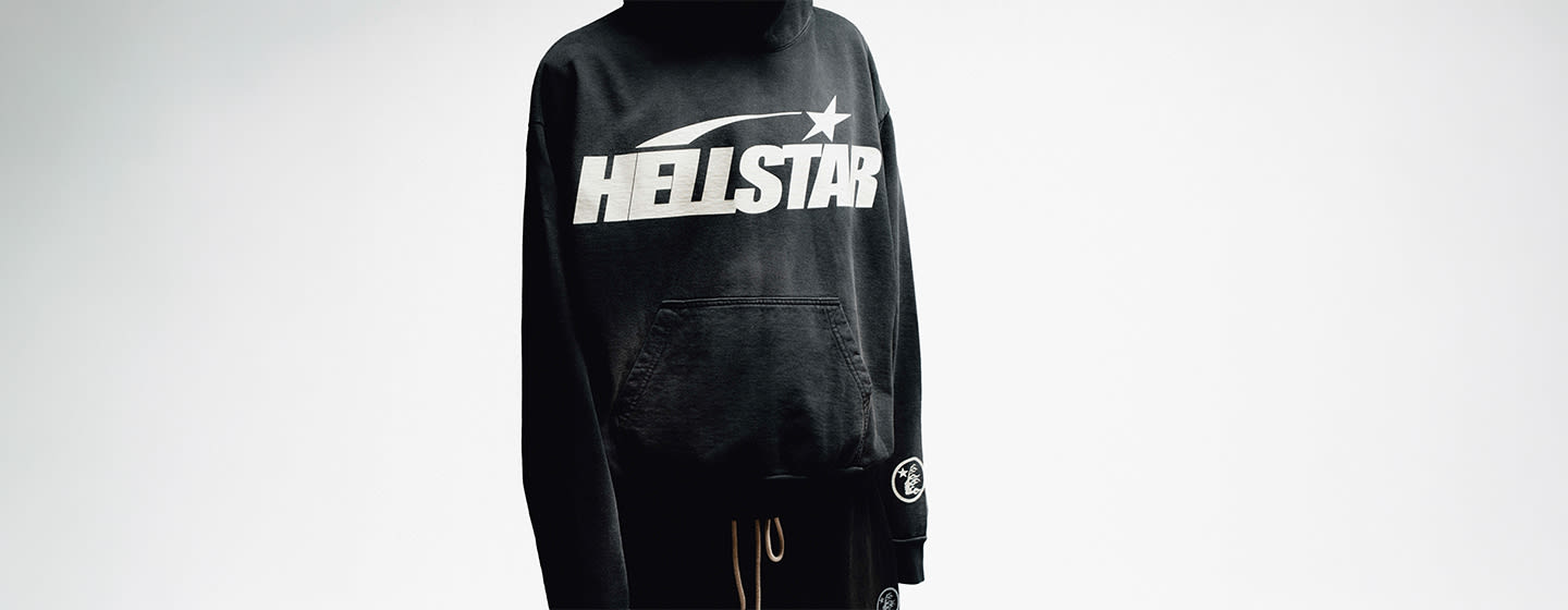 Person wearing a black Hellstar hoodie with an oversized white Hellstar logo across the chest, styled with black pants against a white background.  Mobile: