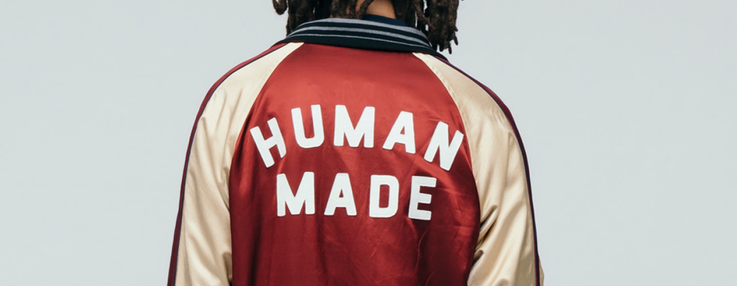 A person seen from behind wearing a satin varsity-style jacket with bold “HUMAN MADE” lettering across the back.