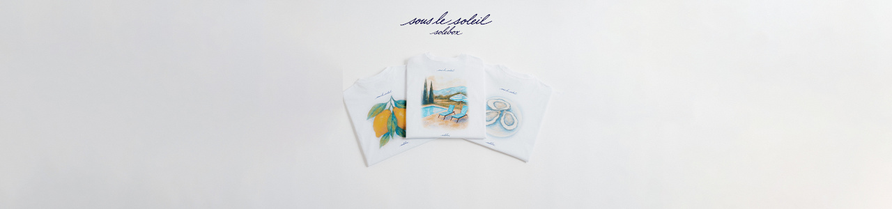 Three folded white T-shirts laid out side by side, each featuring a colorful illustration: lemons on the left, a poolside scene with chairs and umbrella in the center, and oysters on the right. And a slogan in blue which says "sous le soleil solebox