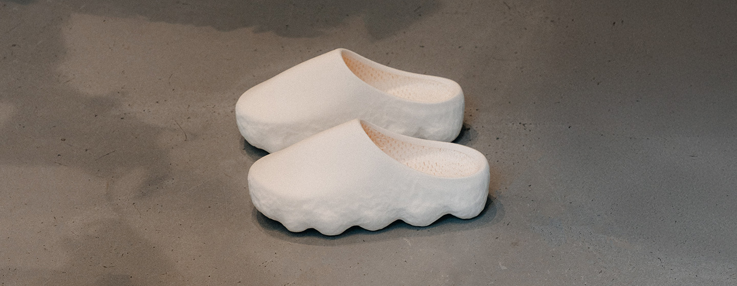 "A pair of minimalist, off-white slip-on clogs with a wavy, textured sole placed on a concrete floor."