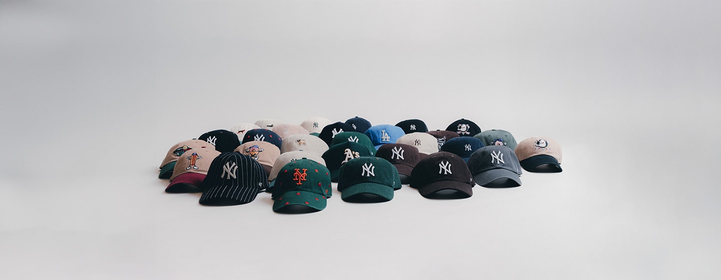 A wide display of various baseball caps arranged in rows on a white surface, featuring logos from teams like the New York Yankees, New York Mets, Los Angeles Dodgers, Oakland A’s, and more.