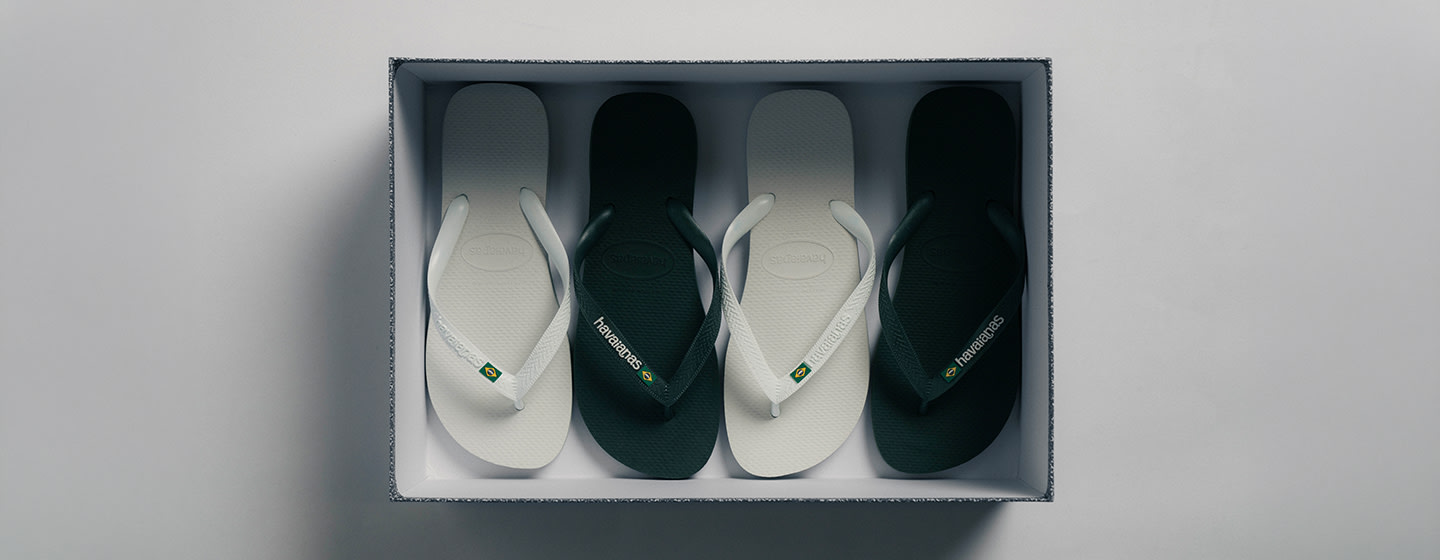 Top view of multiple Havaianas flip-flops in black and white neatly arranged inside a rectangular box, shown against a clean, minimal background.