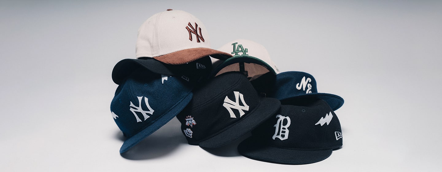 Stack of New Era baseball caps featuring New York Yankees, Los Angeles Dodgers, and Detroit Tigers logos in navy, black, white, and beige colorways, displayed against a clean studio background.