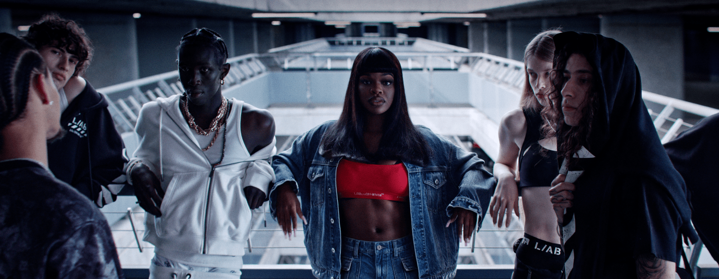 Group of models wearing Off-White™ L/AB apparel in a futuristic architectural setting, showcasing layered denim, sportswear, and technical silhouettes with a bold contemporary aesthetic.