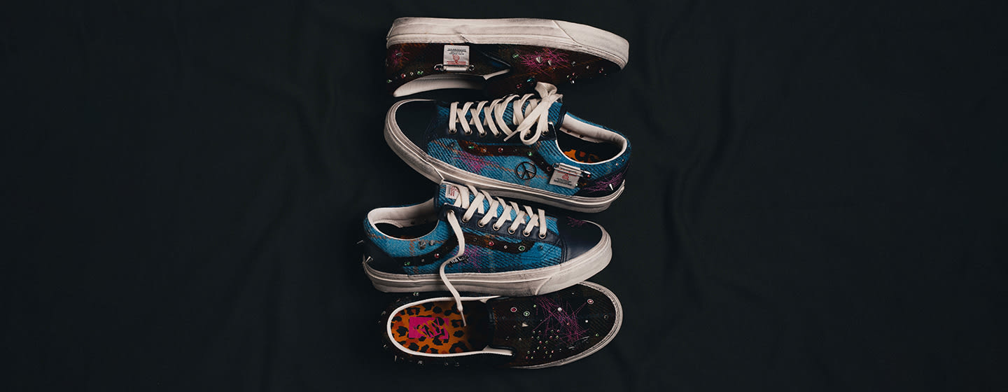 Stacked Vans x Harris Tweed sneakers featuring blue and dark tweed uppers, embroidered details, metal embellishments, and white midsoles against a black backdrop.