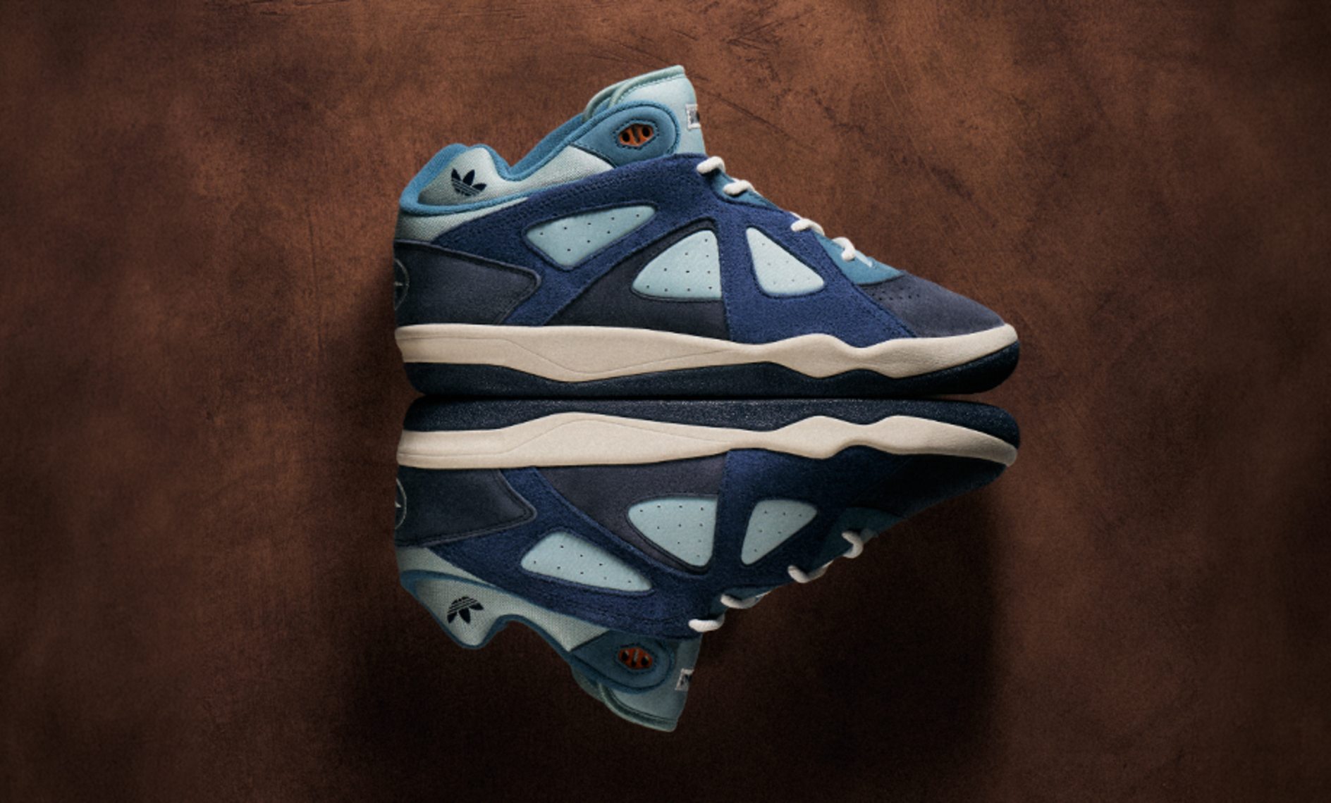 adidas x Bad Bunny Badbo 1.0 "Night Navy" sneaker in dark navy and light blue suede and leather, shown in side profile against a textured brown background.
