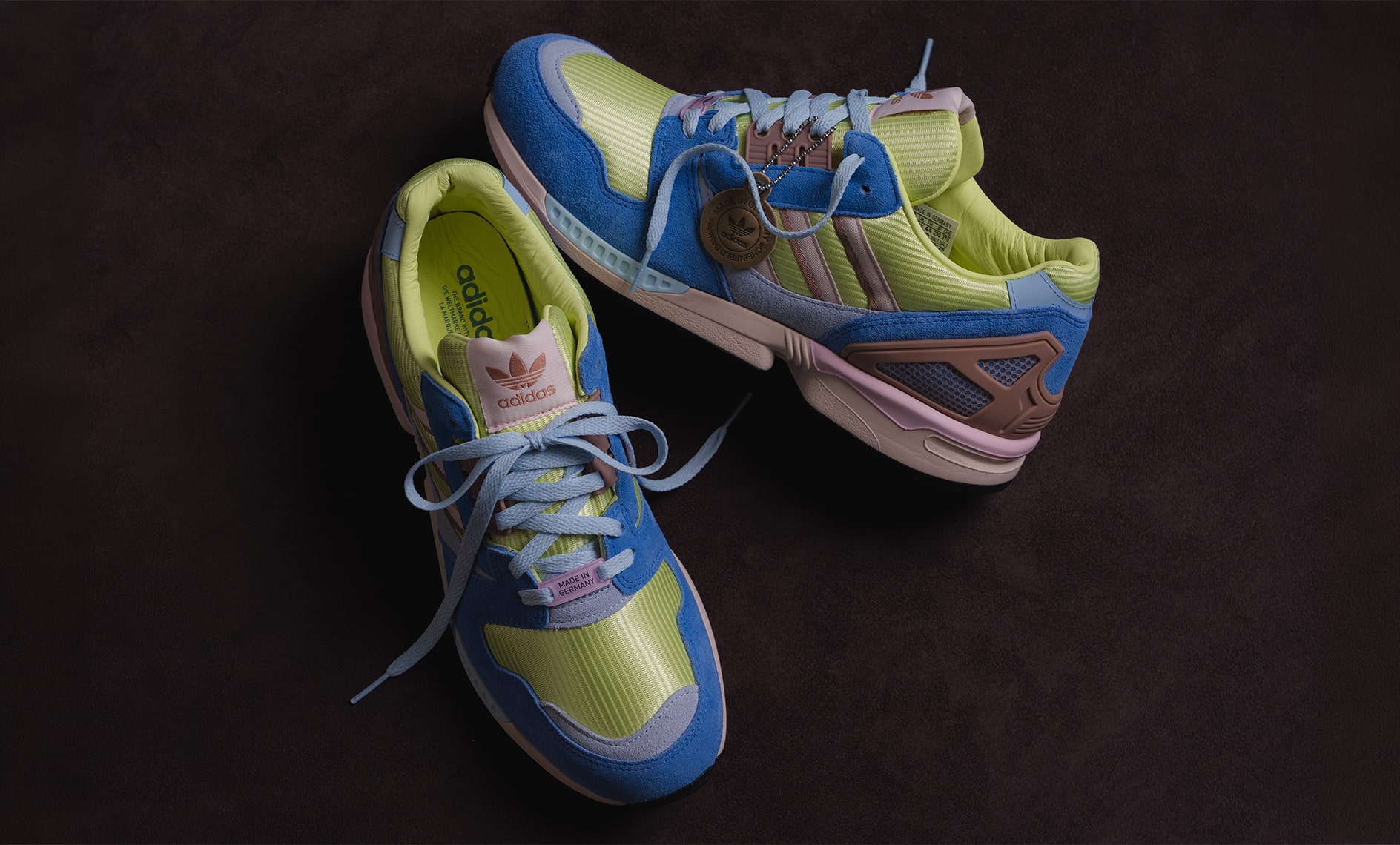 Adidas ZX8000 sneakers in blue suede and neon yellow mesh with pastel pink details, displayed on a dark textured surface.