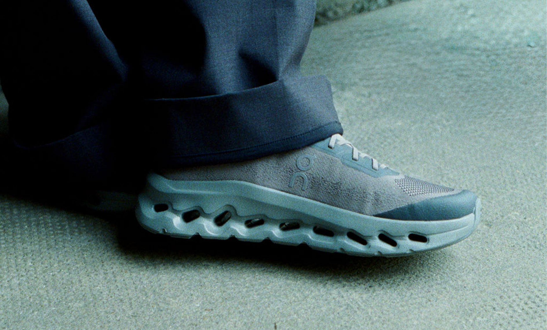 On Cloudtilt sneaker in grey worn with wide-leg trousers on a concrete surface.