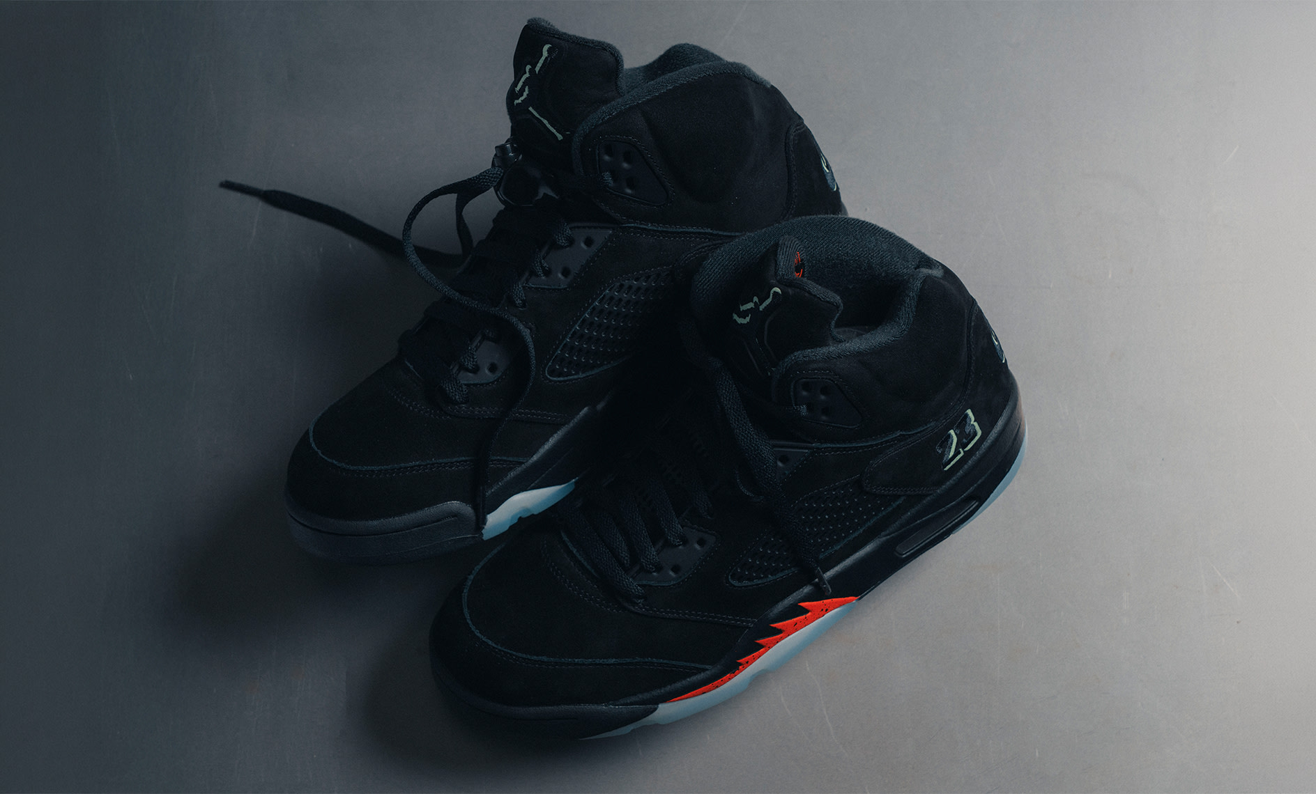 Air Jordan 5 Retro "Halloween" sneakers in black with reflective details and bright orange accents, photographed on a metallic surface.
