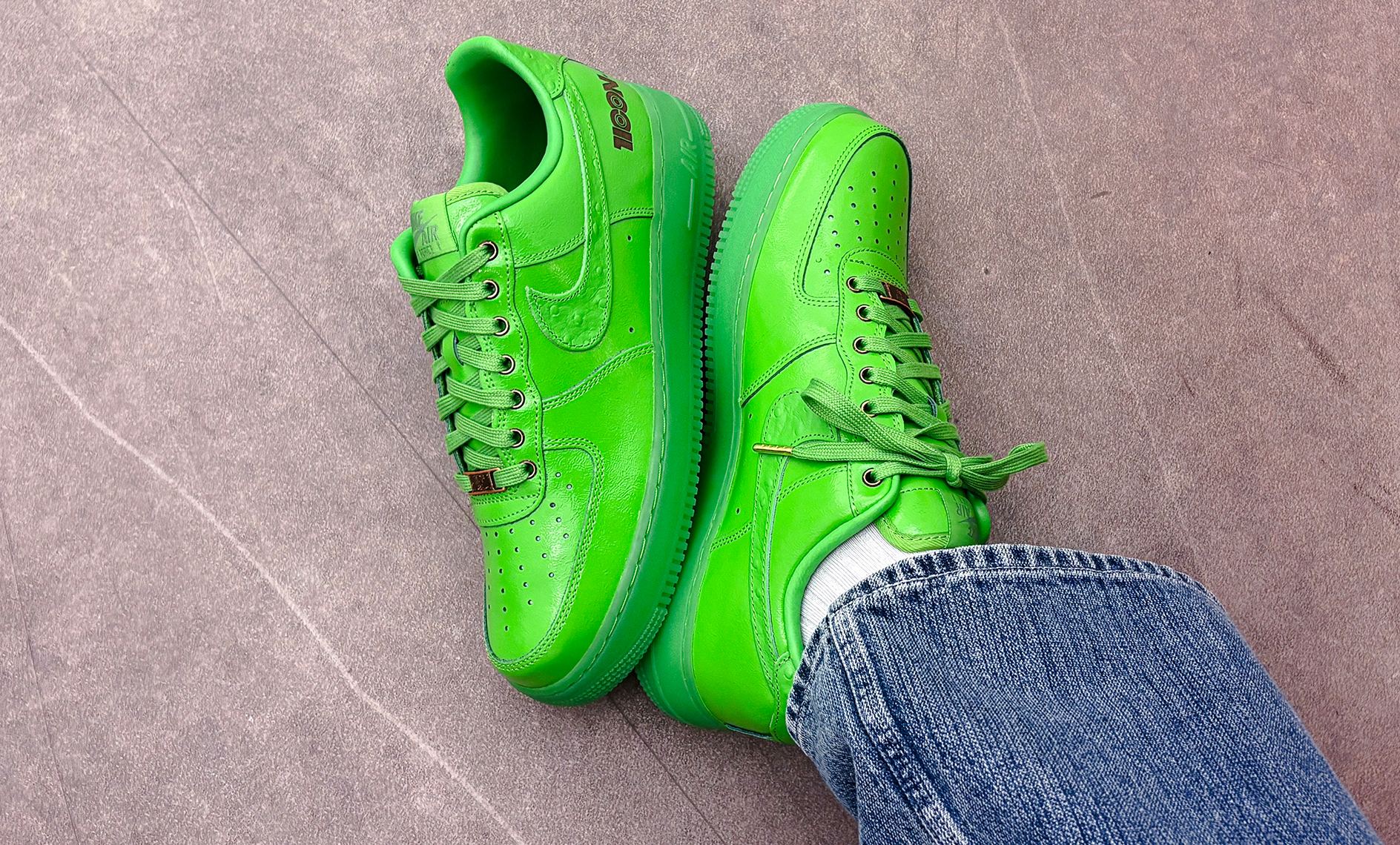 Nike Air Force 1 Low LX “Icon” in bright green leather with tonal Swoosh and laces, worn with blue denim jeans on a gray floor.