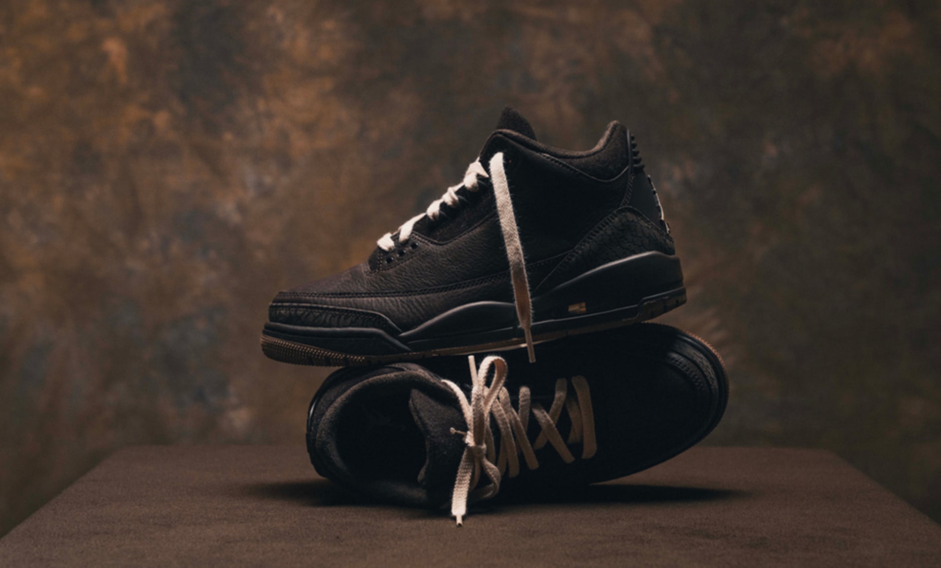 Air Jordan 3 Retro "Fireside" CK9246-200 in black leather with tonal elephant print details, photographed in a premium studio setting with warm brown backdrop and stacked sneaker composition
