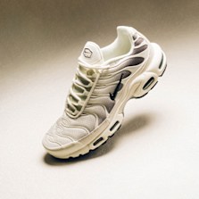 Close-up of a beige Nike Air MaxPlus sneaker with black detailing, floating against a neutral background.