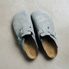 Light grey suede Birkenstock Boston clogs with adjustable straps on a smooth floor.