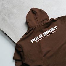 "Brown Polo Sport Ralph Lauren hoodie laid flat, showcasing the brand’s white printed logo on the back."