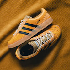 adidas Bad Bunny Gazelle in yellow with black 3-Stripes and white laces on a yellow fabric background.