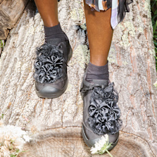 KEEN x Collina Strada Jasper "Rocks" sneakers in black with oversized floral-inspired textile appliqués, worn while standing on a tree trunk outdoors.