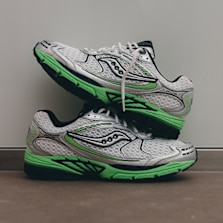 Two Saucony ProGrid Ride 1 running shoes in white mesh with green and black accents, stacked against a light grey background.